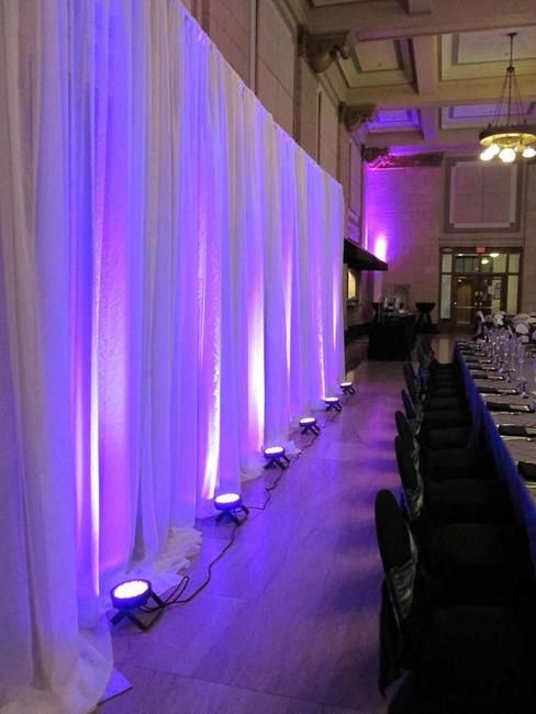 An event space that has been dramatically styled with draping and uplighting, likely for a wedding reception or gala.