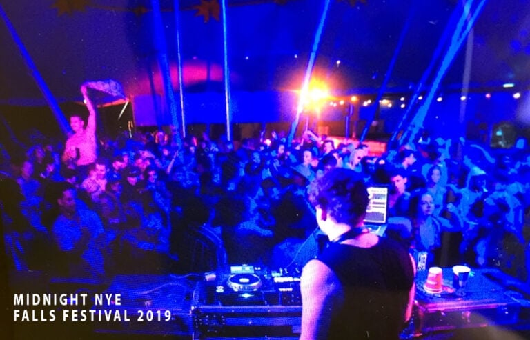A DJ set at a large music festival or New Year's Eve event, dominated by dramatic blue and purple lighting.