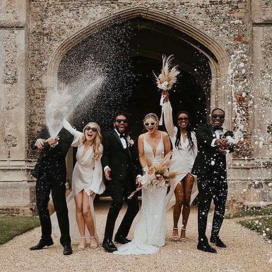 A wedding party posing in front of an old, arched stone building, possibly a church or manor house.