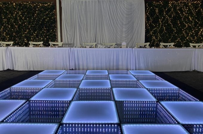 An elegantly set event space, likely for a wedding reception or gala, featuring a striking LED dance floor.