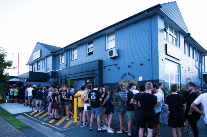 A large crowd of young people waiting in a long line outside a two-story building.